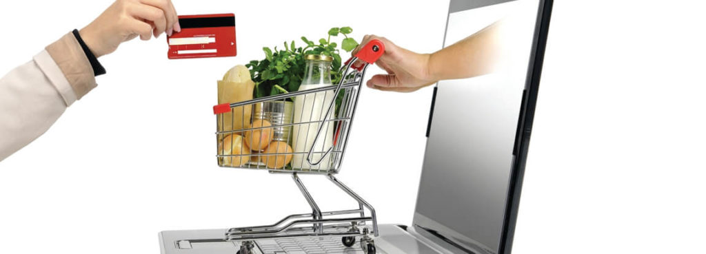 A person holding a shopping cart and a credit card in front of a laptop